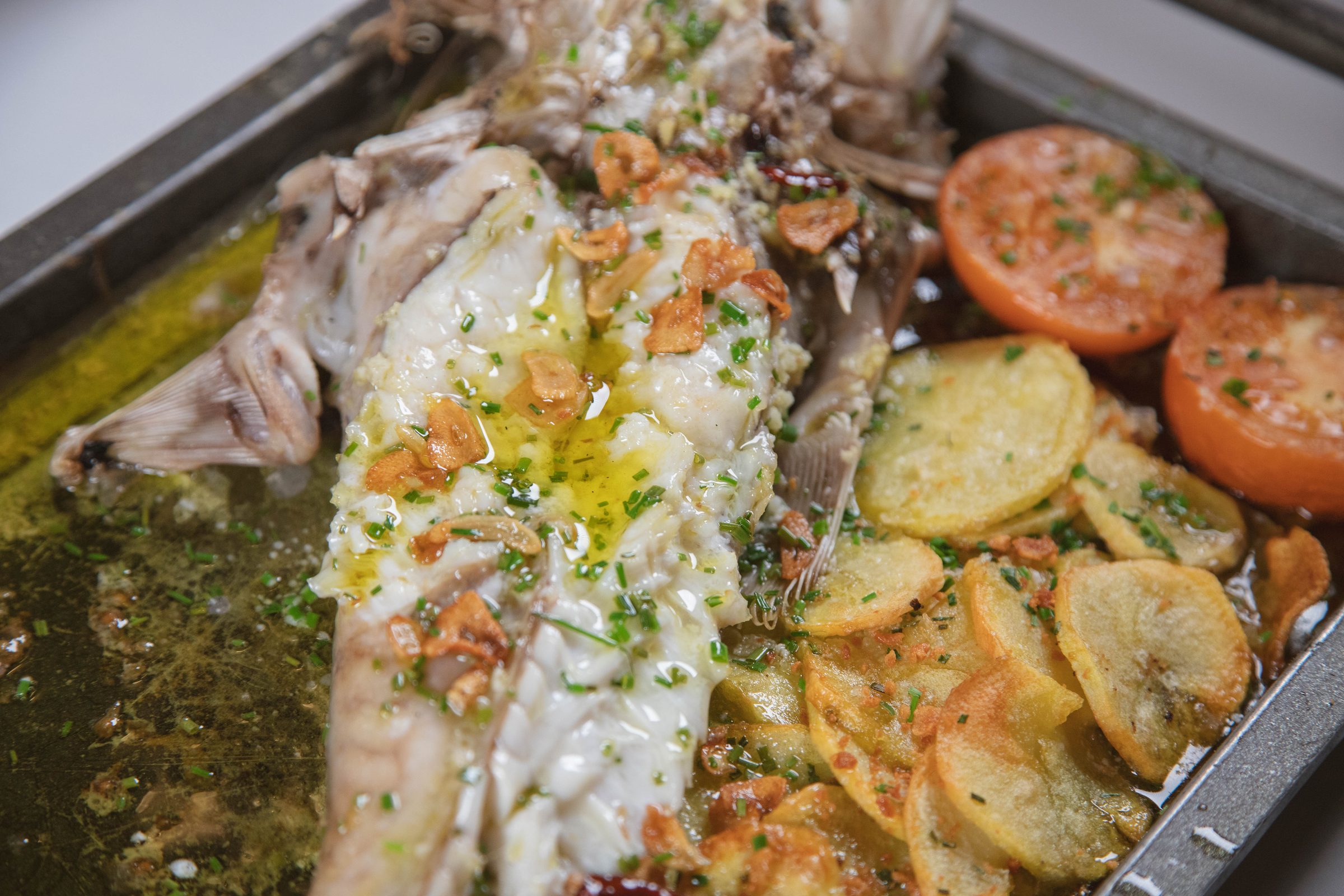 Pescado abierto al horno en bandeja, con patatas panadera y tomate asado